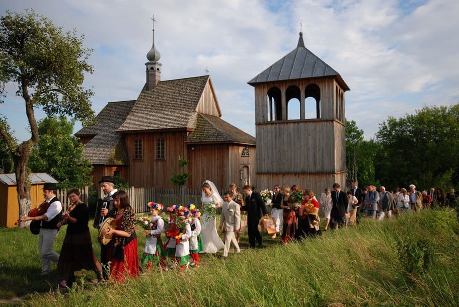 Radosne wesele w malowniczej okolicy z drewnianym kościołem.