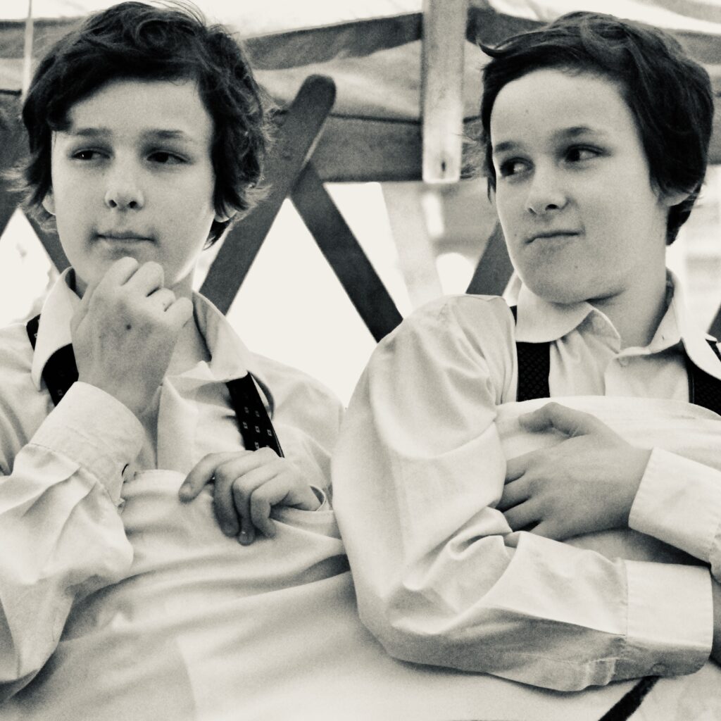 Dwóch chłopców w białych koszulach, na tle drewna.