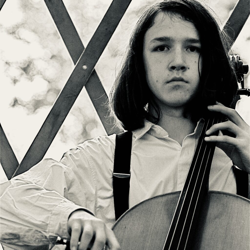 Młody muzyk grający na wiolonczeli w parku.