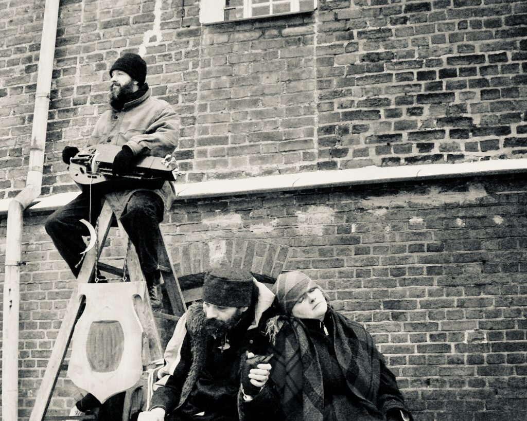 Muzykant na drabinie, dwie osoby siedzące w tle.