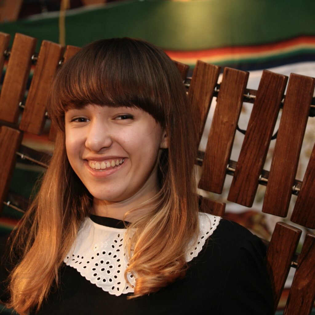 Młoda kobieta z uśmiechem, w czarnym płaszczu.