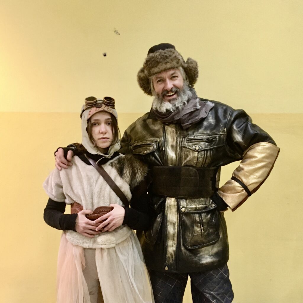 Dwoje osób w kostiumach przy jasnej ścianie.