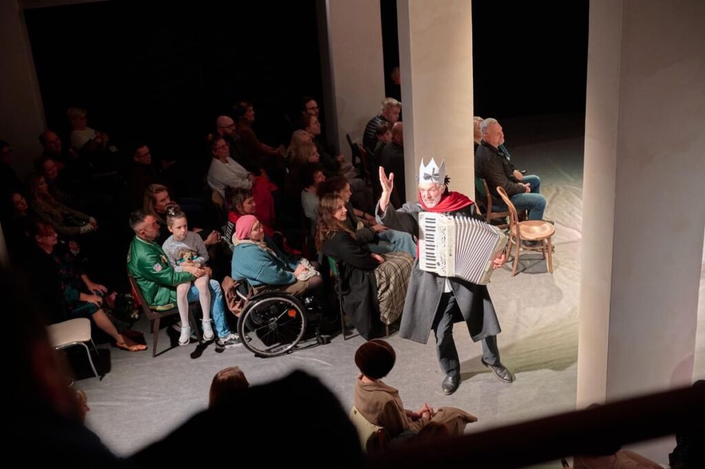 Mężczyzna w koronie gra na akordeonie, publiczność.