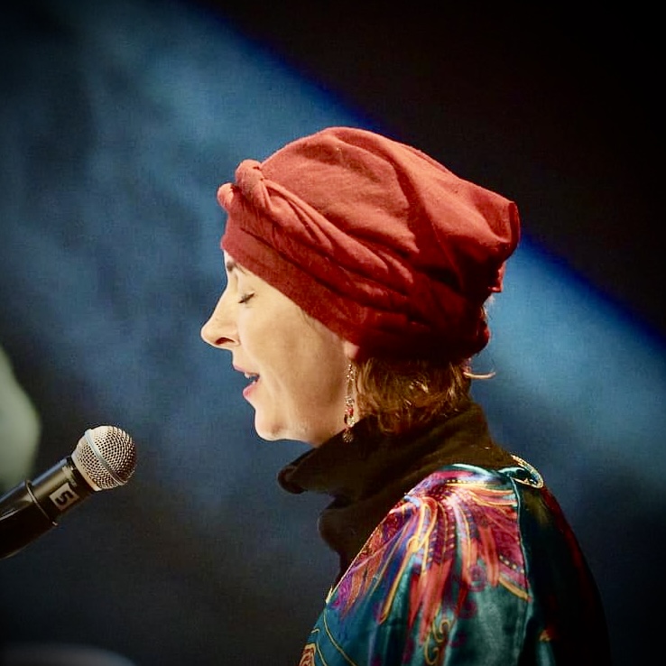 Kobieta w kolorowej bluzce śpiewa do mikrofonu.