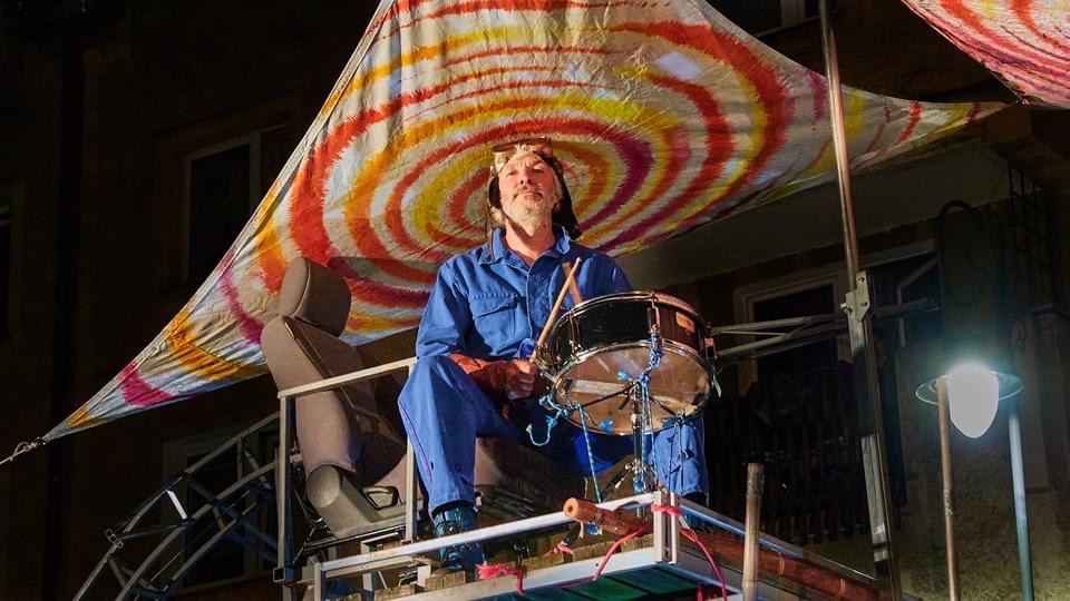 Muzyk grający na bębnie pod kolorowymi plandekami