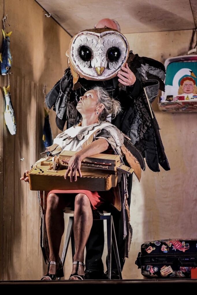 Teatr: postaci z sową i instrumentem na scenie.