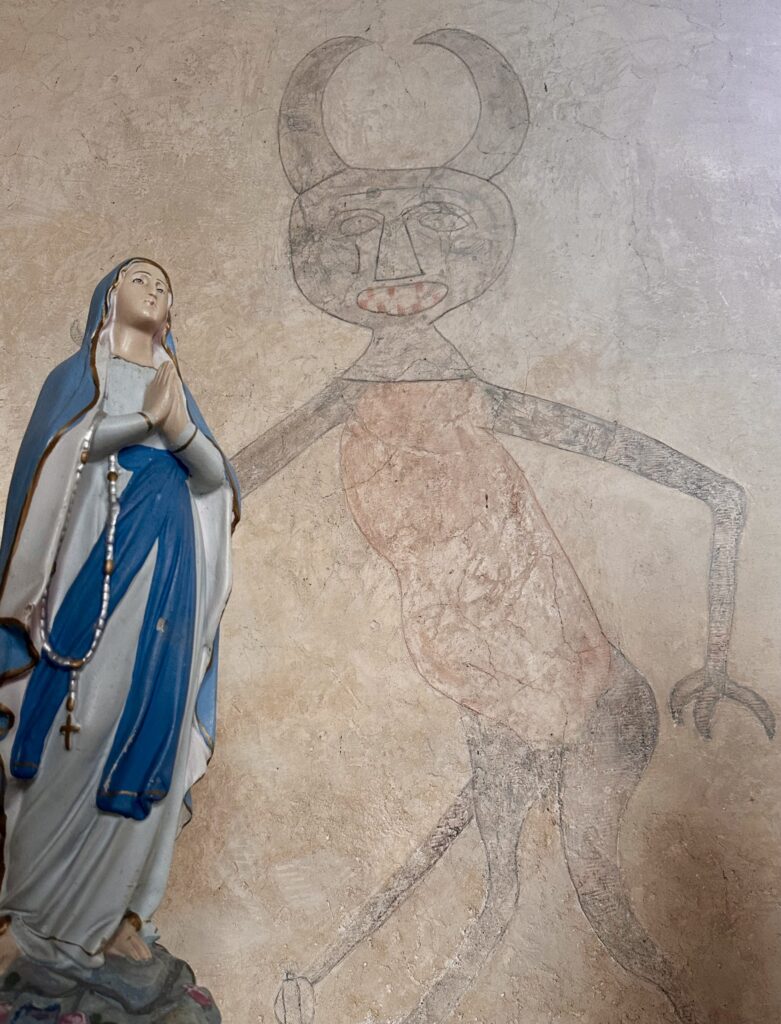 Figurka Maryi i mural z postacią demonopodobną.