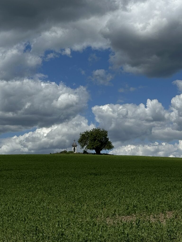 Kapliczka na zielonym wzgórzu pod chmurami.