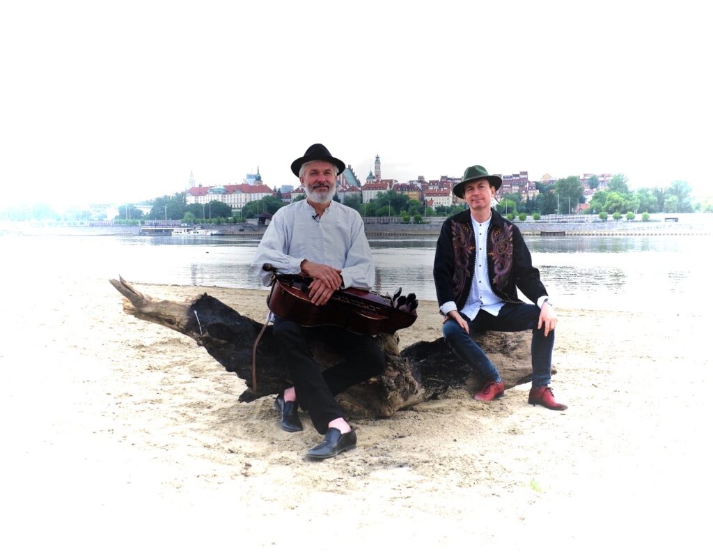 Dwaj muzycy na plaży przy rzece.